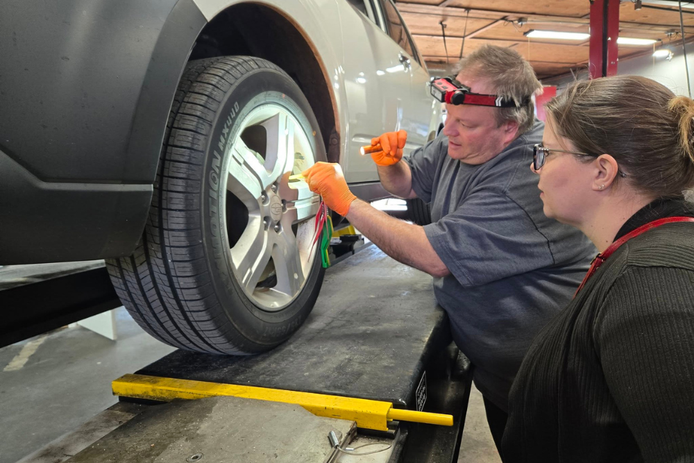 Brake repair in summerville, SC. SBS Automotive Maintenance and Repair. Image of a technician explaining tire alignment readings to a customer while the vehicle is lifted, emphasizing accuracy, safety, and performance.